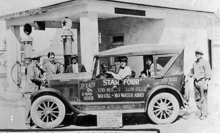 A grayscale image of an old vehicle with people